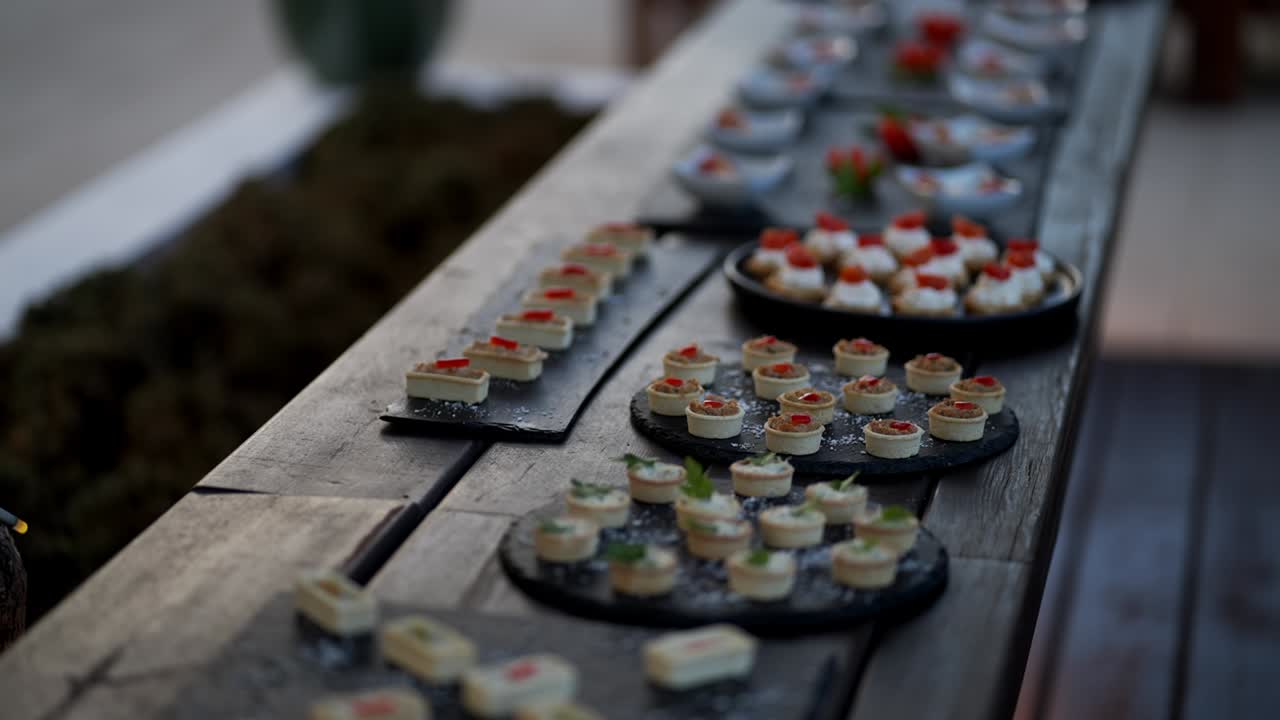 rustic wooden table filled with assorted gourmet canapés served on dark platters