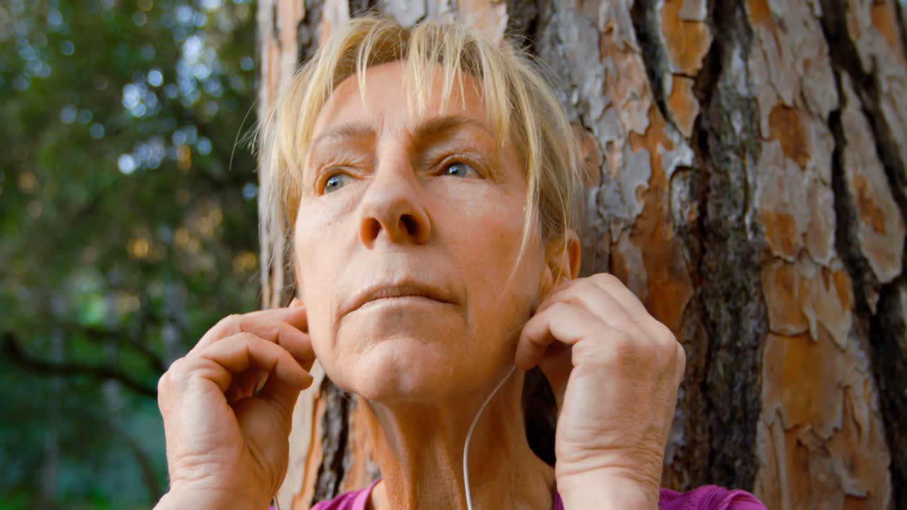 mujer mayor apoyada en un árbol y escuchando música 4k