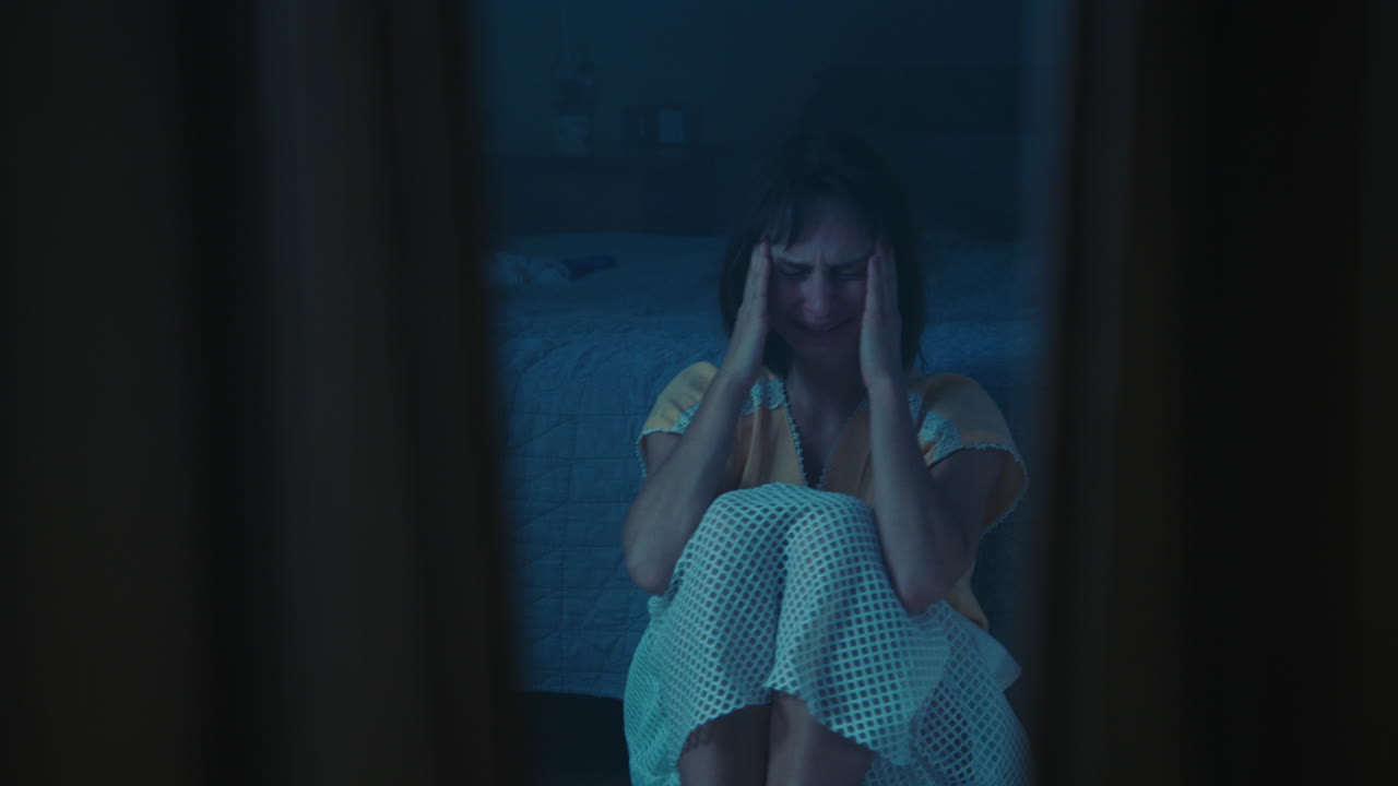 Una ragazza traumatizzata e disorientata siede sul pavimento della camera da letto.