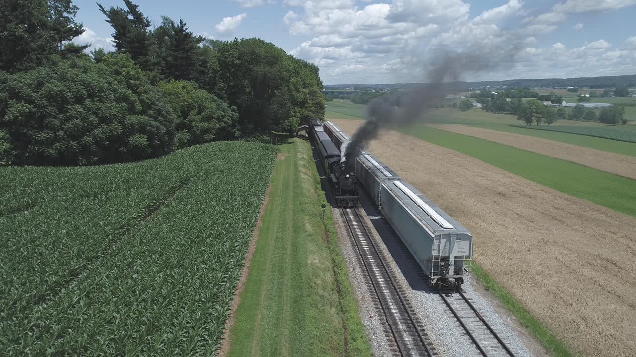 화창한 여름날 시작하기 위해 부풀어 오르는 빈티지 증기 기차가 있는 농지와 시골의 공중 전망