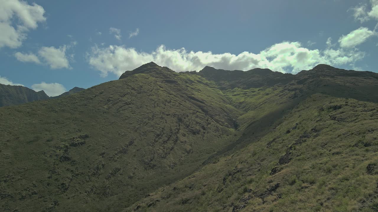 Vista aerea di una ripida catena montuosa contro un cielo blu e nuvole.