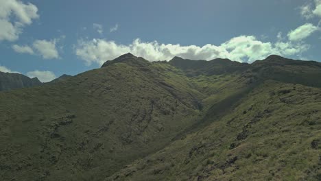 Aerial-view-of-steep-mountain-range-against-blue-sky-and-clouds