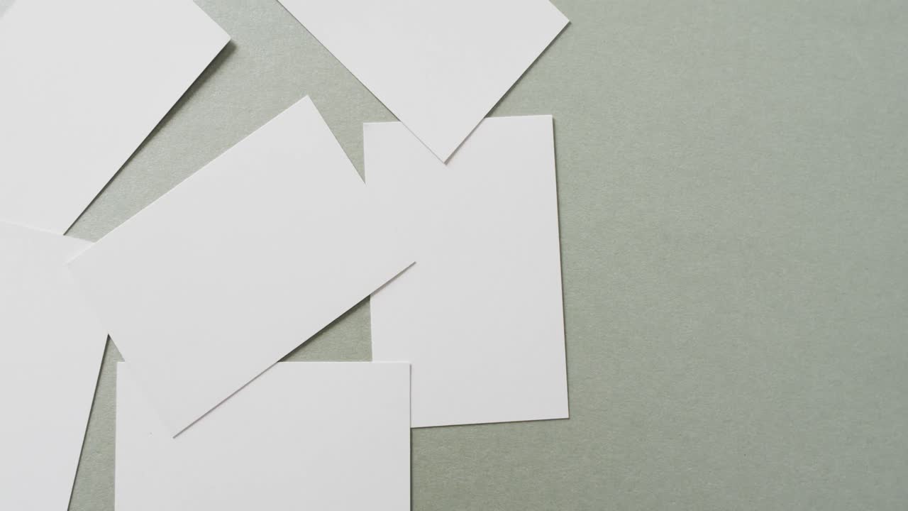 Multiple blank white business cards on green background, copy space, slow motion