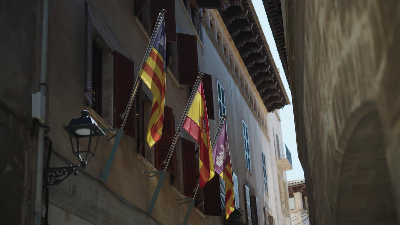 Three flags hanging on a building's balcony in a narrow street