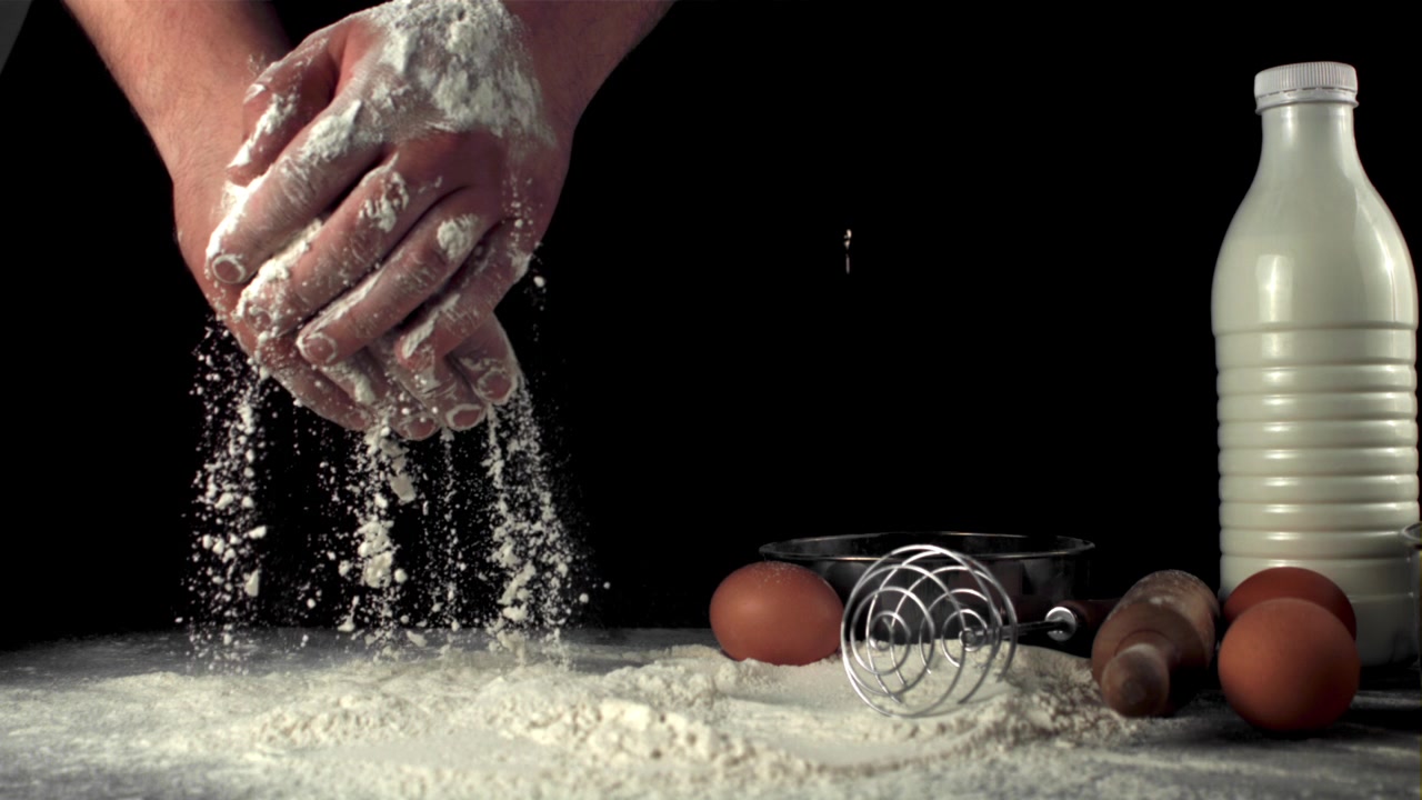 Tangan Koki Mengayak Tepung dengan Bahan-bahan Kue di Latar Belakang Hitam
