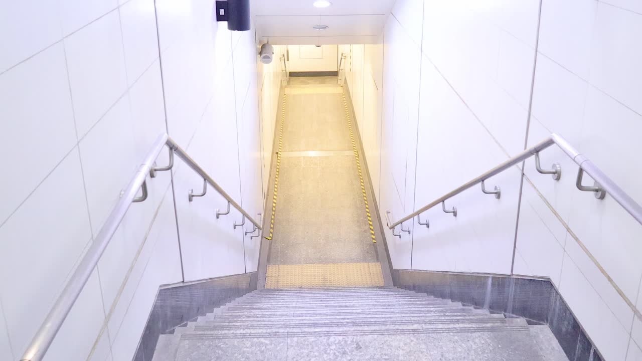 A sequence of frames showing a well-lit, empty subway stairwell with clean, white walls and metal railings