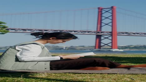 woman reading in a park by the bridge