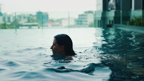 woman swimming in a rooftop pool with a city view