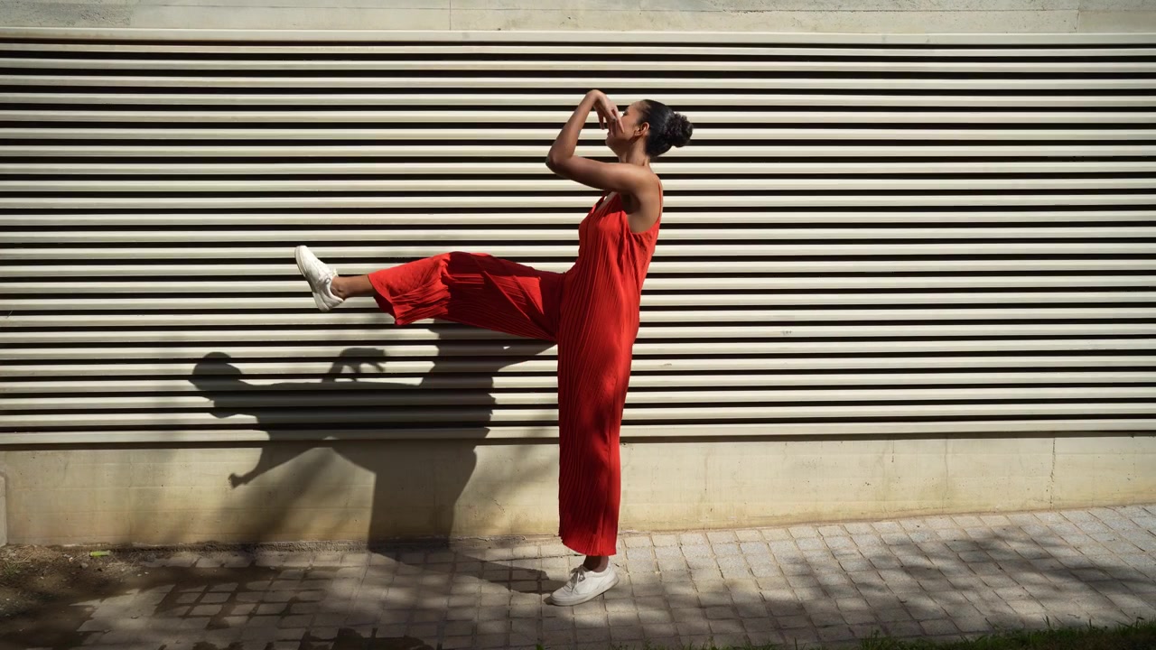 Una donna alla moda in una sorprendente tuta rossa posa elegantemente contro un muro pittoresco