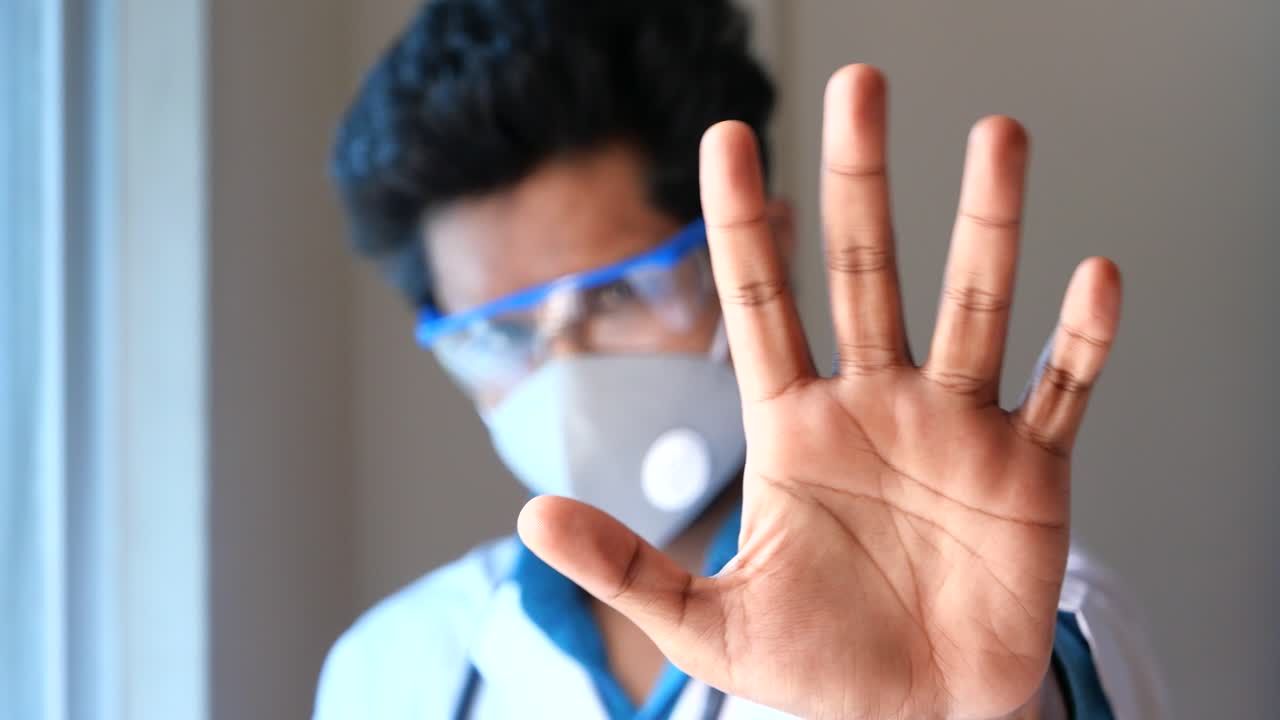 Medico che fa il gesto di stop con equipaggiamento protettivo