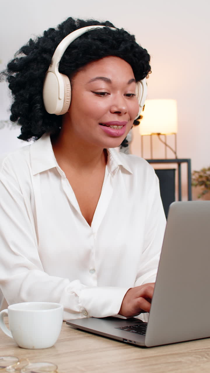 Donna d'affari afroamericana con cuffie wireless lavora al laptop sorridendo e godendosi la musica oggi