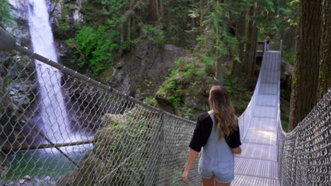 woman crossing old traditional bridge in forest in british columbia bc, canada with waterfall and river