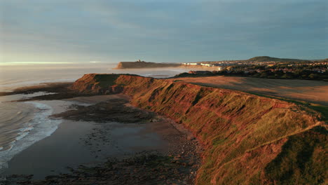 Establishing-Aerial-Drone-Shot-of-Cleveland-Way-at-Golden-Hour-at-Low-Tide-with-Scarborough-Castle-in-Background