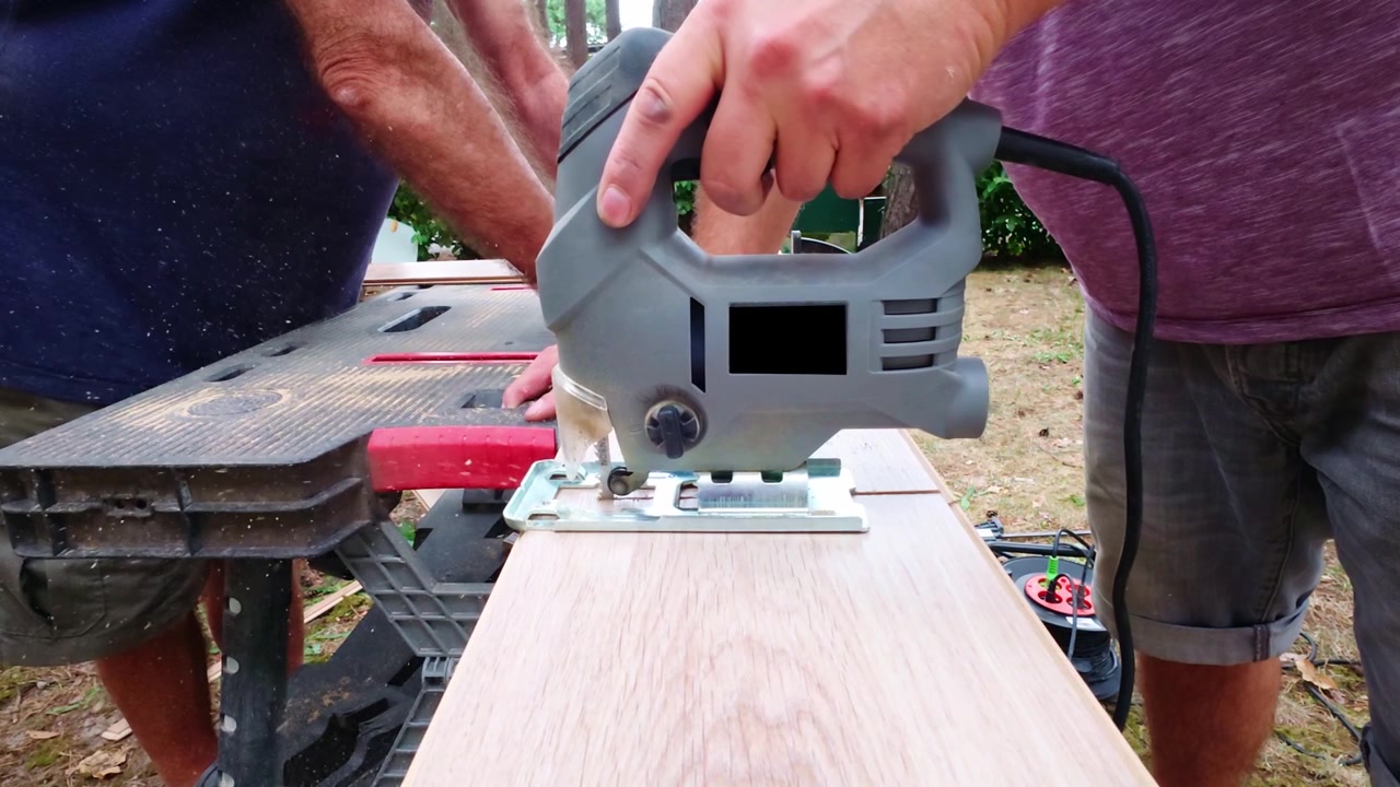 Two professional carpenters cutting wooden laminate floor planks with electric jigsaw, faceless home Improvement concept.