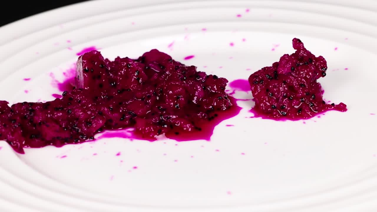 Close-up of vibrant dragon fruit pulp spread across a white plate, highlighting its rich color and texture.