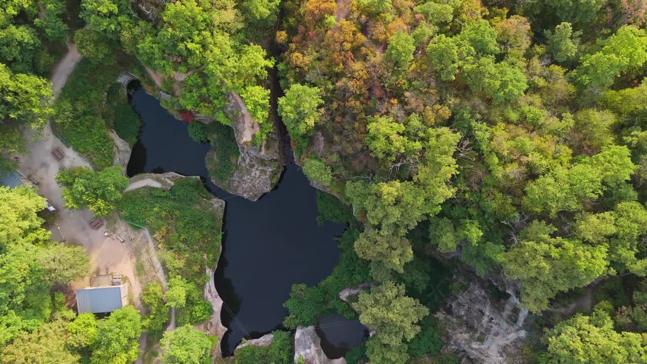 Tilt-down drone view of the Tarn of Megyer-hegy near Sárospatak, Hungary, revealing a beautiful lake surrounded by lush greenery and forest within a historic millstone quarry turned nature preserve