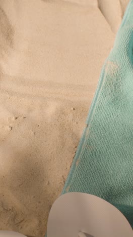 Vertical-Video-Summer-Holiday-Concept-Of-Beach-Towel-With-Flip-Flops-Sunglasses-And-Camera-Against-Sand