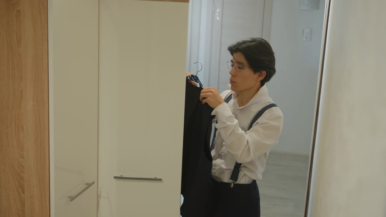 Esame delicato del guardaroba. Uomo asiatico che sceglie con cura i capi in uno spazio moderno. L'individuo valuta attentamente le opzioni di abbigliamento in un ambiente contemporaneo con la sicurezza di uno stilista.