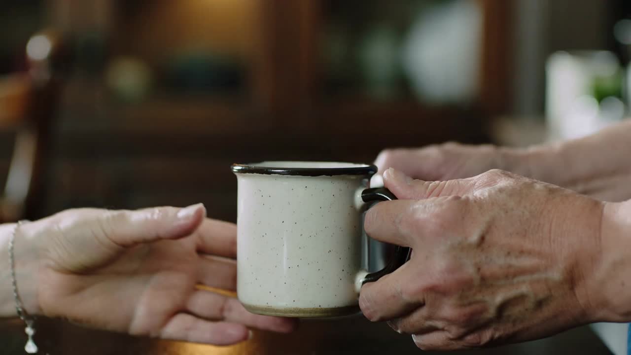 Tipping mug, veined partner pouring into partner's enamel mug at home, bracelet letting partner sip
