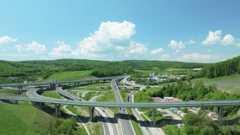 an aerial drone moves forward above an intricate tangle of a highway junction, showcasing cars navigating complex roundabouts and intersecting roads