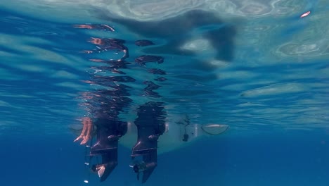 slow motion under water footage of legs and feet in sea water beneath surface hanging from speedboat ladder