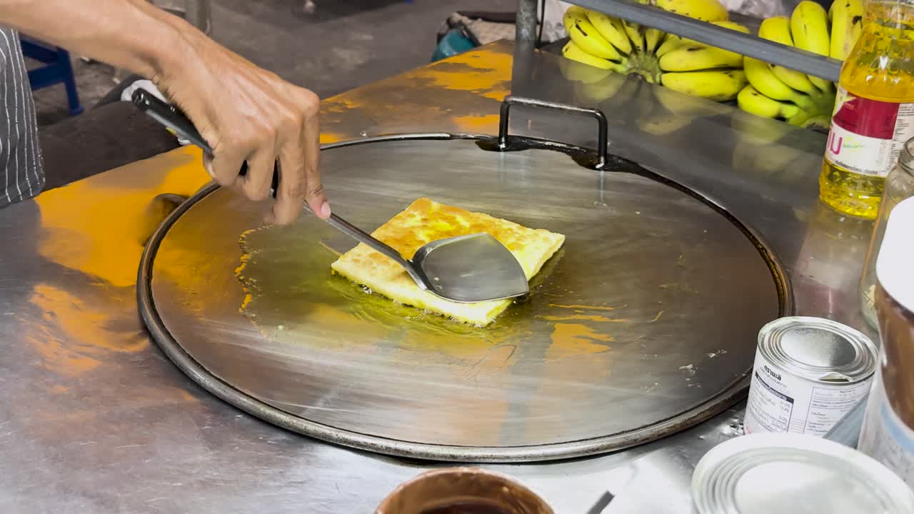 un vendedor callejero prepara hábilmente roti tailandés en una parrilla caliente en phuket, mostrando técnicas tradicionales de comida callejera