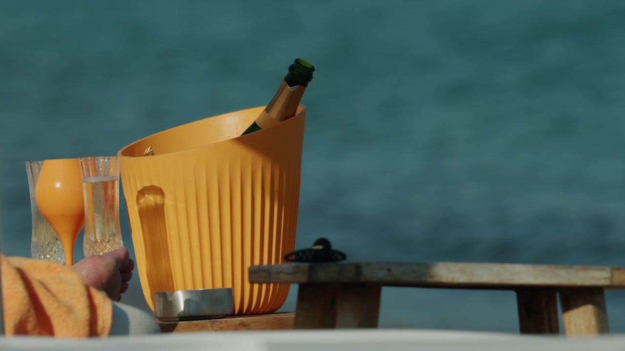 Bottiglia di champagne in fresco in un secchiello per il ghiaccio con bicchieri su un tavolo di legno, godendosi un lussuoso tempo libero in riva all'oceano.