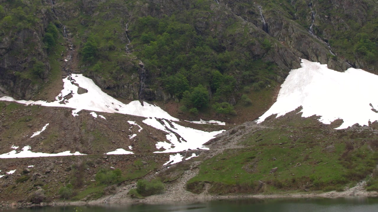 En sakte panorering over steinete fjellsider med smeltende snøflekker og grønn vegetasjon