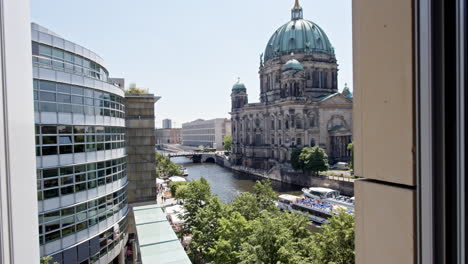 Scenic-video-of-Berlin-showcasing-the-Spree-River,-Berliner-Dom,-and-modern-glass-buildings,-with-a-ship-passing-by-under-a-cloudless-sky-in-Germany