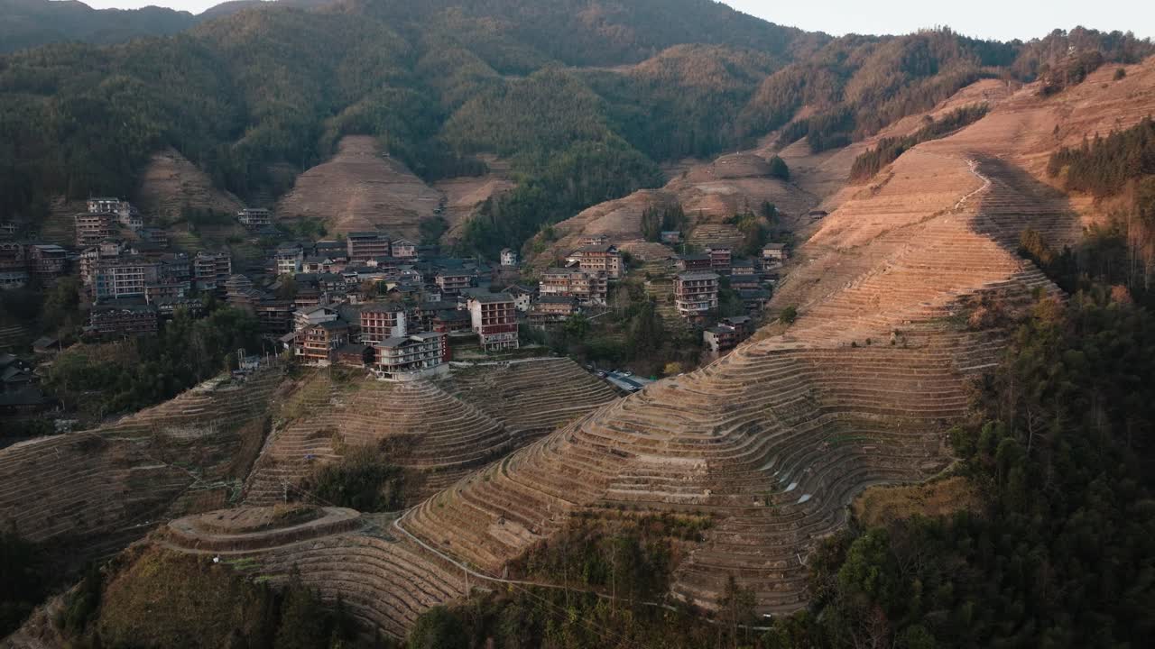 Widok z drona na wioskę Longsheng otoczoną tarasowymi wzgórzami i zalesionymi zboczami w ciepłym, złotym świetle w pobliżu Guilin, Guangxi, Chiny