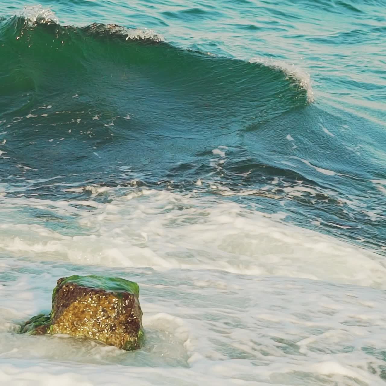 high sea waves of turquoise color are crashing on the rocks and turning into foam. Slow motion