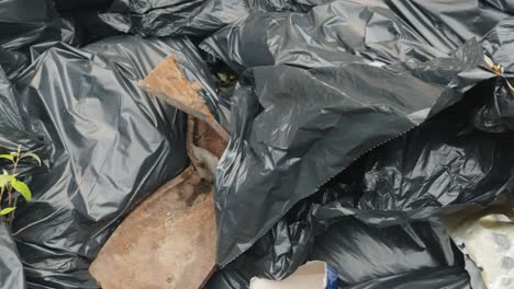 dolly close up across a pile of trash in garbage bags at a local dump