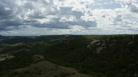 Dolly-in-aerial-drone-shot-of-the-beautiful-green-and-rocky-countryside-of-Sítio-Novo,-Brazil-in-the-state-of-Rio-Grande-do-Norte-with-farmland-surrounding-below-on-a-warm-sunny-summer-day