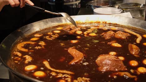 hand holding a ladle stirring and mixing meat and eggs in this thick soup called kai palo-egg and pork chinese style, accepted thai food, bangkok, thailand