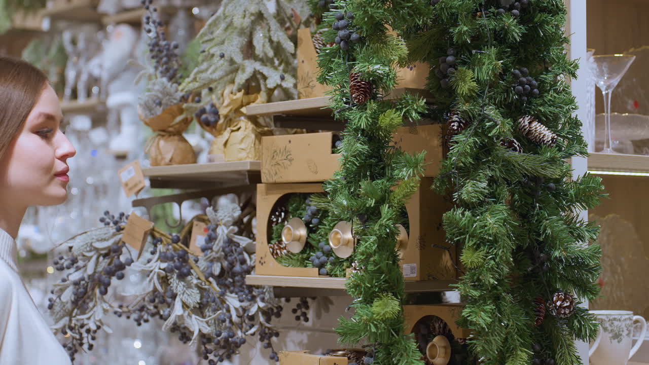 Lady admiring beautiful hanging tinsel in festive decorated shop, surrounded by pinecones, greenery, and ornaments, creating warm holiday atmosphere in a well-lit store