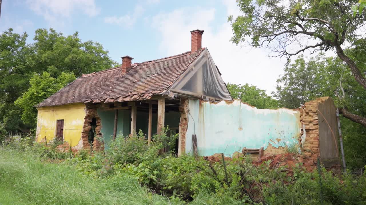 Old, abandoned house with a broken roof and walls surrounded by overgrown vegetation
