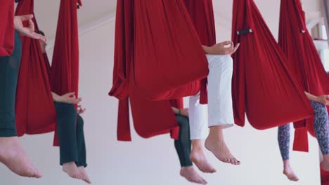 women legs with bare feet hang down from fly yoga hammocks