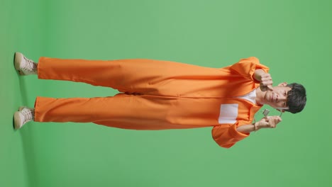 full body of asian male prisoner standing on the green screen background, showing the handcuffs and pointing his finger towards you