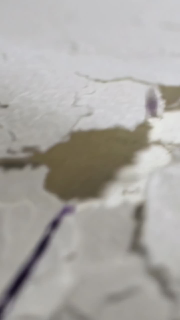 Vertical video: Falling black droplet merging into pool on cracked plaster, spreading ink trails