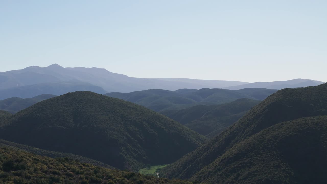 A breathtaking view of the Klein Karoo mountain range, Western Cape, South Africa, bathed in bright sunlight. The clear blue skies accentuate the rugged terrain and expansive, majestic peaks