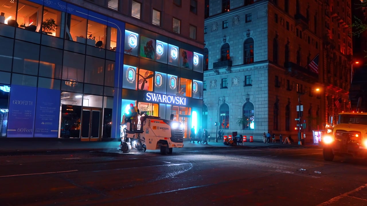New York, USA, 15 aprile 2026: Lavori stradali fuori dal negozio Swarovski sulla Fifth Avenue di notte. Lavori stradali notturni sulla Fifth Avenue vicino alla vetrina Swarovski con luci di veicoli e facciata in vetro.
