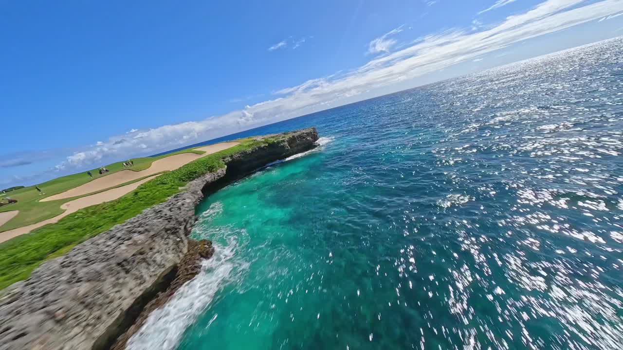 Ripresa aerea veloce lungo la costa di Punta Cana con acqua blu cristallina vicino al campo da golf sotto il sole