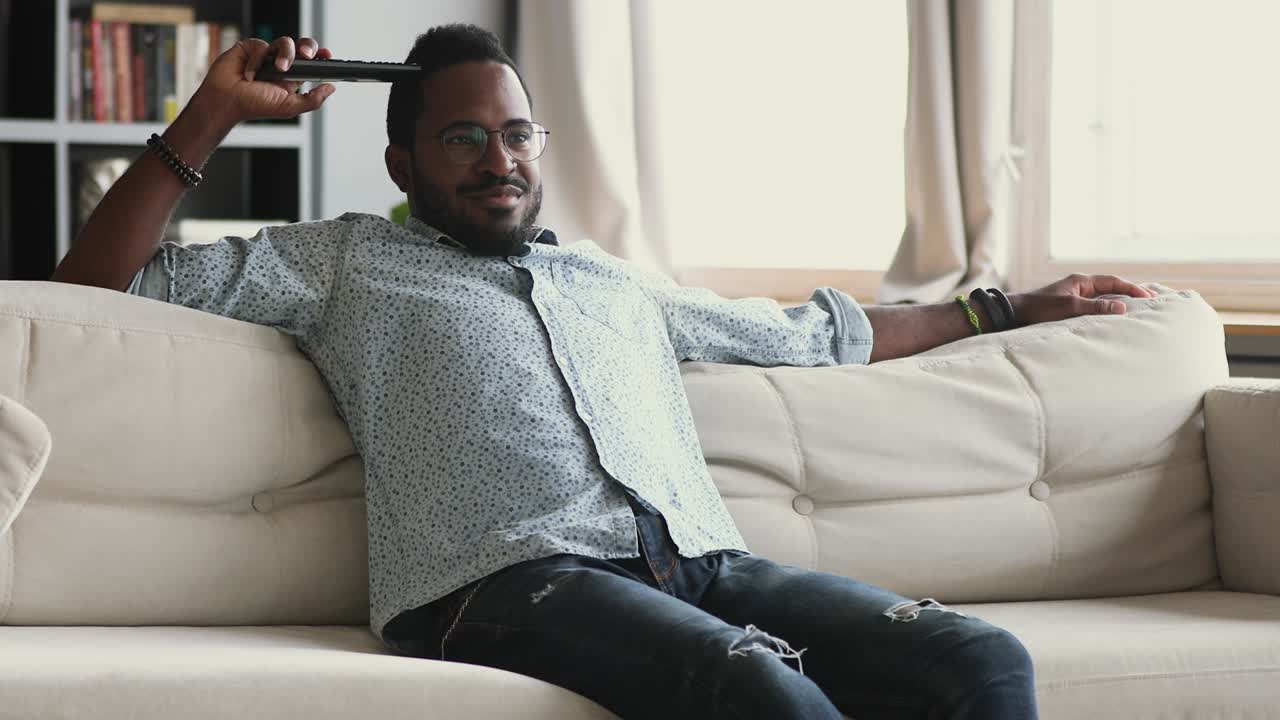 Happy african man hold remote control watching tv at home