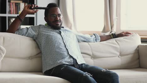 hombre africano feliz con el control remoto viendo la televisión en casa