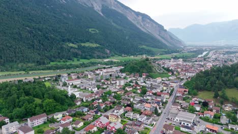 swiss town named domat ems in valley between swiss alps on cloudy day. historic city with houses, homes and church. aerial wide shot. quiet atmosphere in switzerland