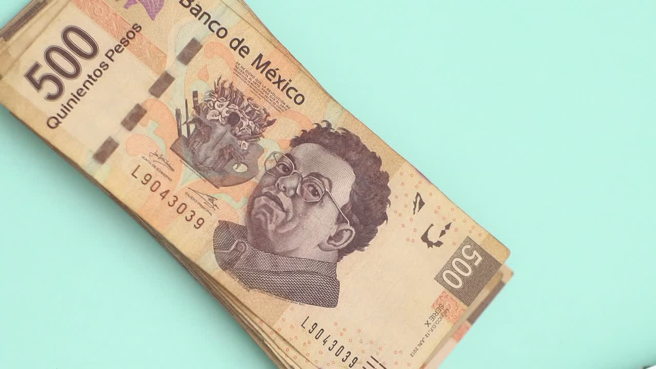 primer plano de la mano colocando una pila de billetes de 500 pesos mexicanos en la mesa azul