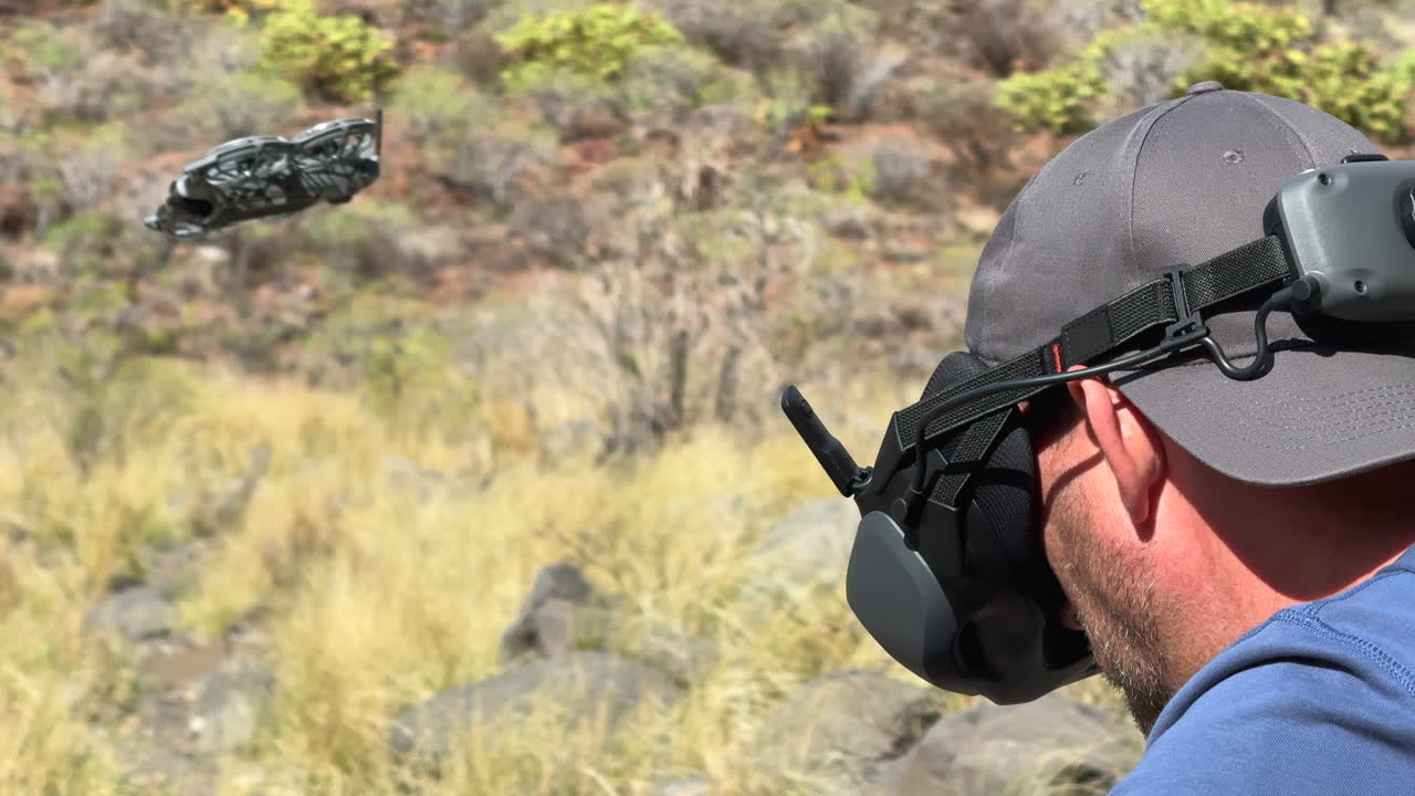 Drone pilot wearing FPV goggles flying a quadcopter in a rocky landscape
