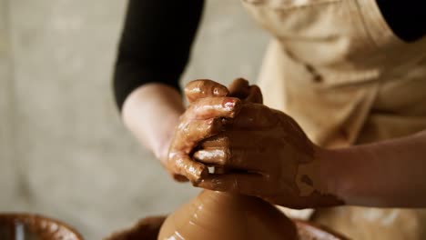 Female-potter's-hands-with-red-manicure-working-with-wet-clay-on-a-pottery-wheel-making-a-clay-product-in-a-workshop.-Unrecognizable-female-person-forming-a-vase,-pulls-up-the-neck