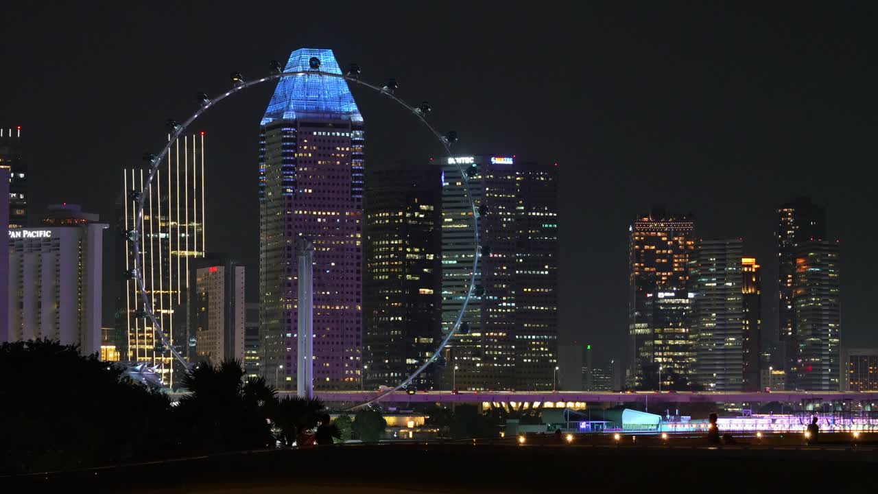 Night downtown cityscape with illuminated high rise buildings featuring landmark Singapore flyer captured at the rooftop park of Marina barrage.