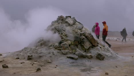 Tourists walk past a steaming geothermal vent in the rugged Namaskaro region of Iceland